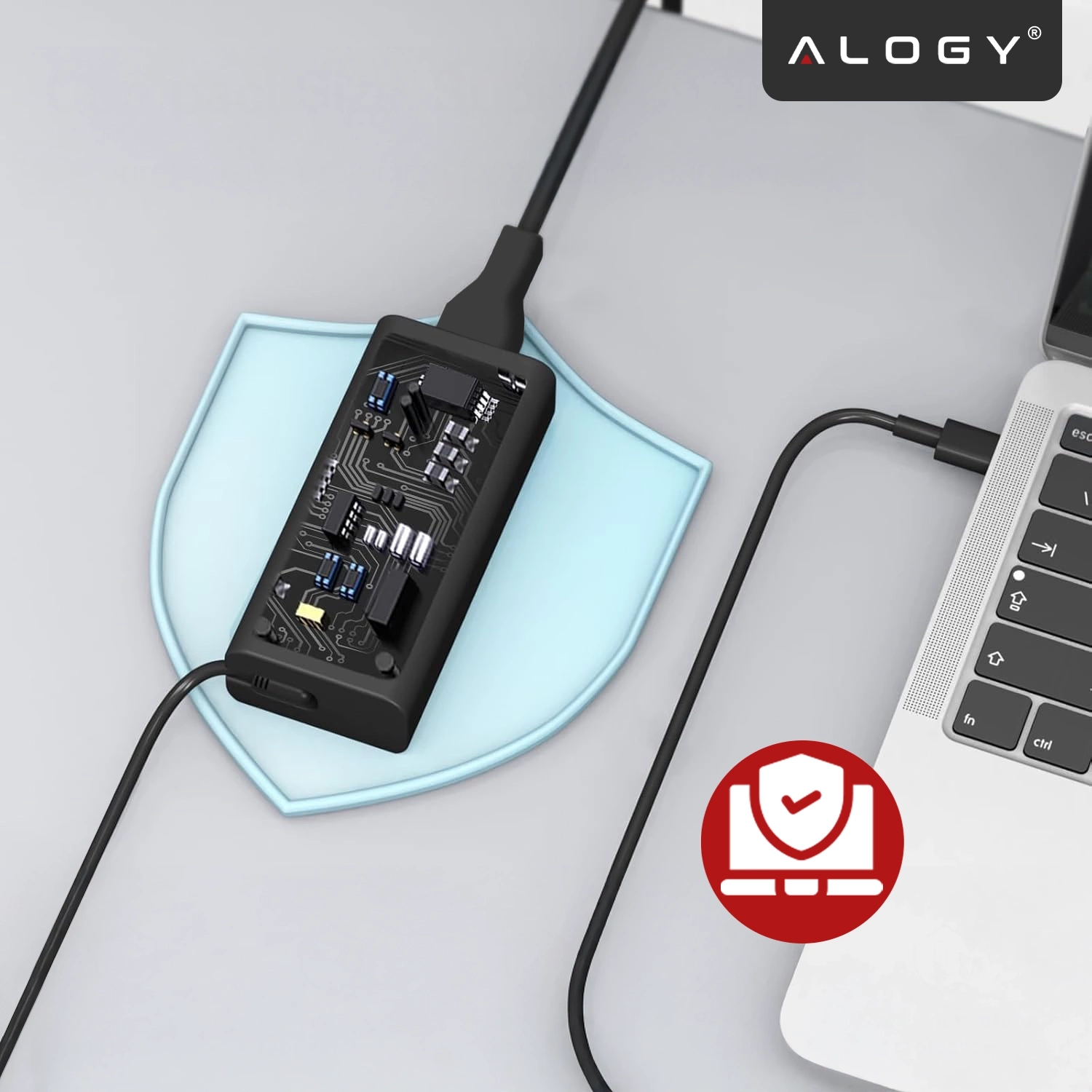 Na obrazie widoczna jest ładowarka zasilacza laptopa z odkrytą elektroniką, podłączona do laptopa. W prawym górnym rogu znajduje się logo \'ALOGY\'.