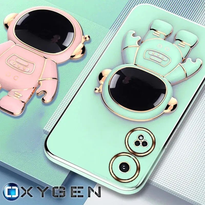 Obraz przedstawia dwa etui na telefon w kształcie astronautów, jedno różowe, drugie miętowe, z dużymi czarnymi wizjerami. W prawym dolnym rogu widoczne jest logo \'OXYGEN\'.