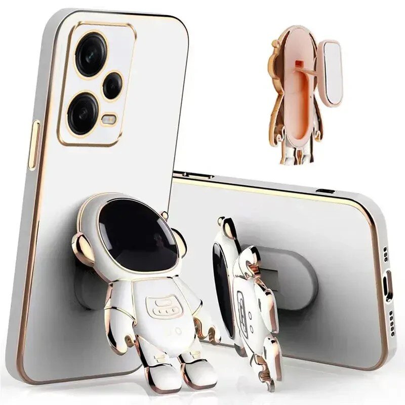 Na obrazie widoczne jest etui na telefon z motywem astronauty, które posiada uchwyt w kształcie postaci. Etui jest w kolorze białym z elementami złotymi, a telefon ma trzy obiektywy aparatu.
