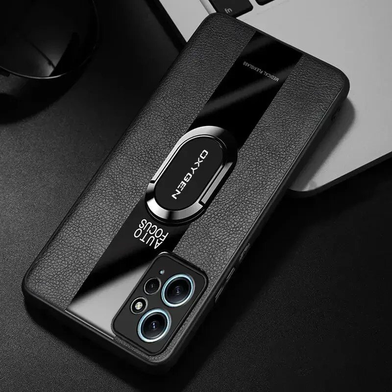 Na obrazie widoczne jest etui na telefon z napisem \'OXYGEN\' oraz \'AUTO FOCUS\', umieszczone na ciemnym tle obok laptopa. Etui ma teksturę przypominającą skórę i posiada metalowy uchwyt.