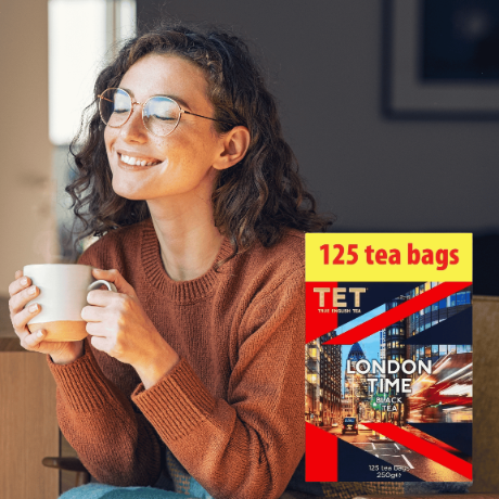 Osoba siedzi z kubkiem w dłoniach, obok widoczne jest opakowanie herbaty z napisem \'TET LONDON TIME BLACK TEA 125 tea bags 250g\'.