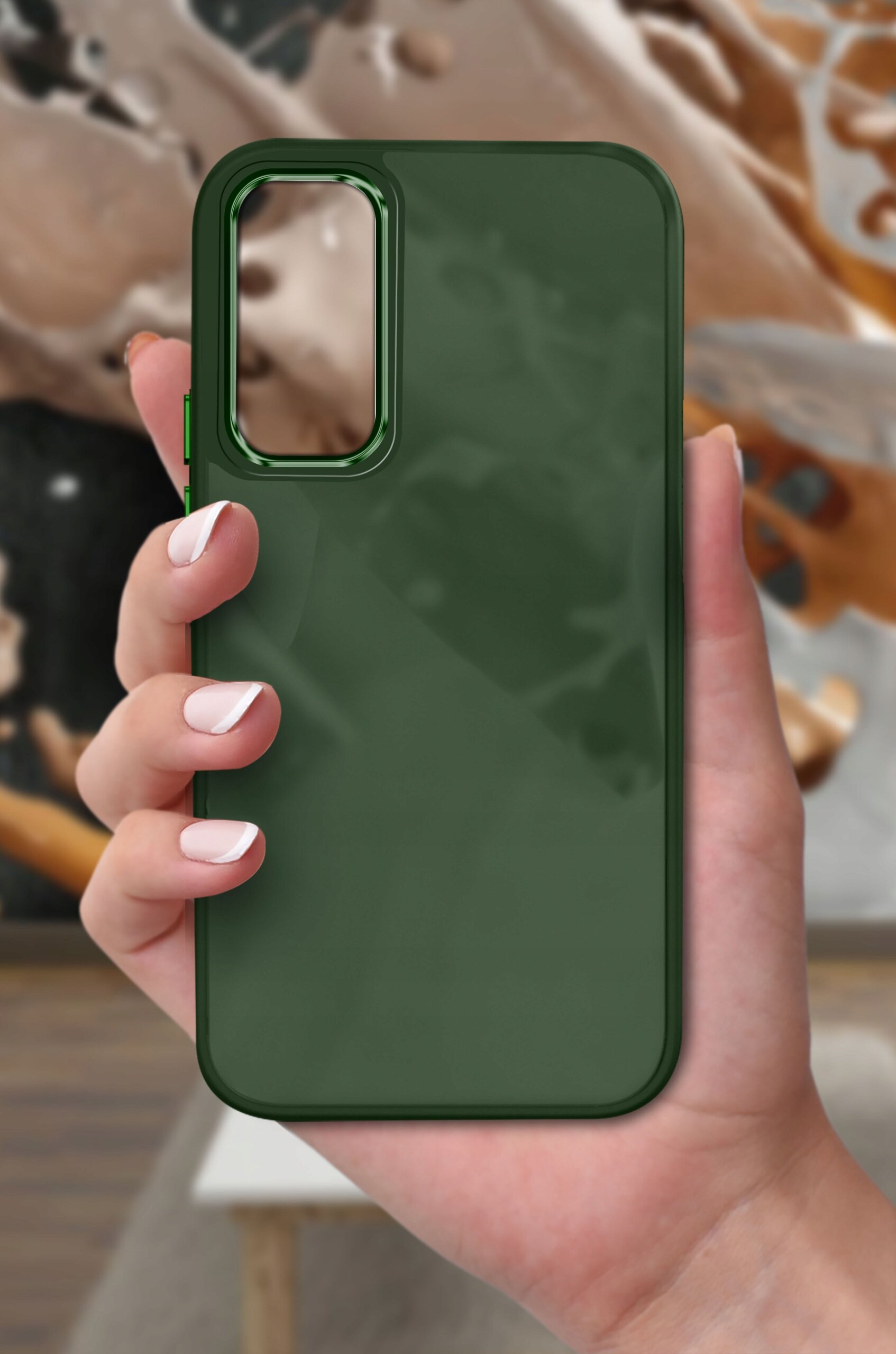 Zielone, matowe etui na telefon trzymane w dłoni, z wycięciem na aparat. W tle widoczna jest rozmyta kompozycja w odcieniach brązu i beżu.