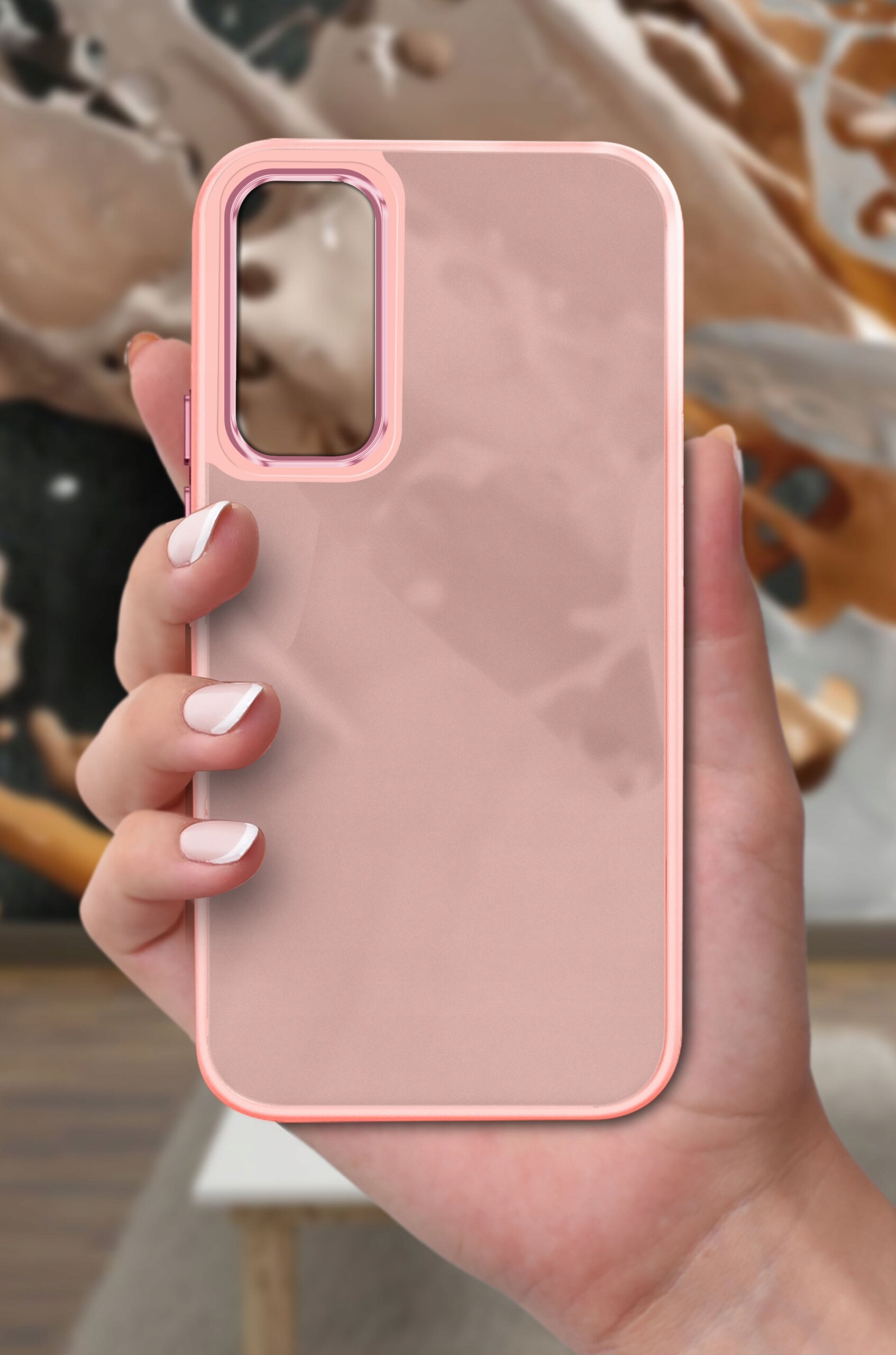 Różowe, matowe etui na telefon trzymane w dłoni, na tle rozmytego, abstrakcyjnego wzoru.