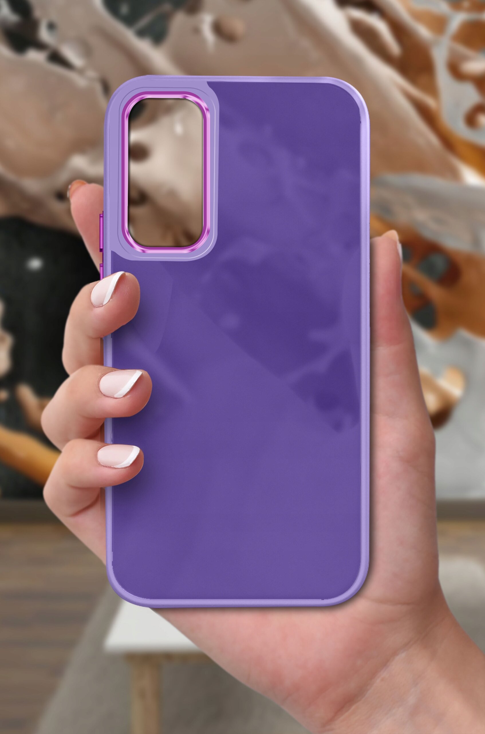 Fioletowe etui na telefon trzymane w dłoni, z wycięciem na aparat w różowym kolorze. W tle widoczna jest rozmyta kompozycja w odcieniach brązu i beżu.