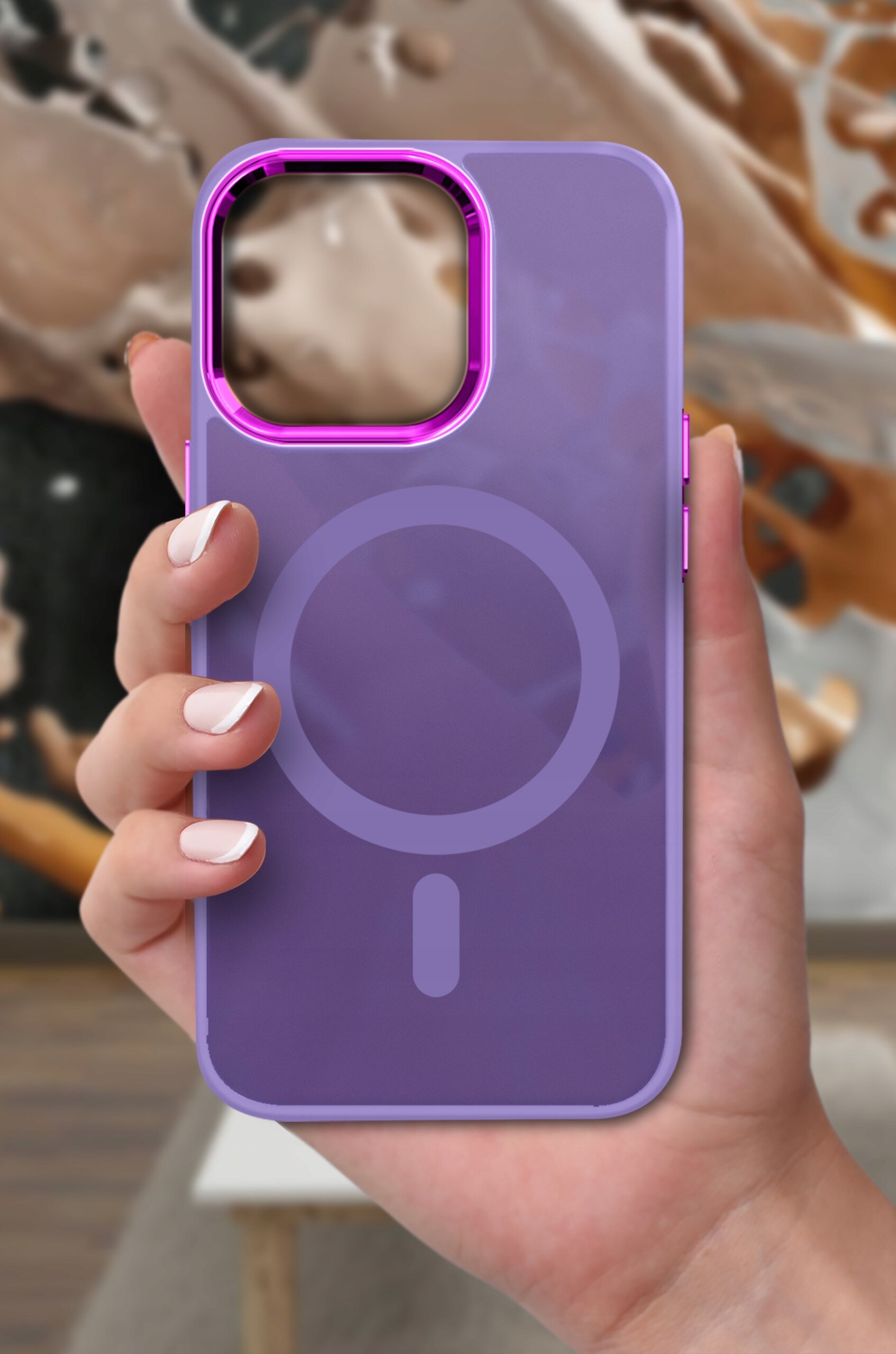 Fioletowe etui na telefon z okrągłym wzorem na środku, trzymane w dłoni na tle rozmytego wnętrza.