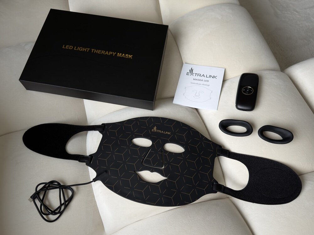 Na obrazie znajduje się czarna maska LED z geometrycznym wzorem, obok której leży czarne pudełko z napisem \'LED LIGHT THERAPY MASK\'. Widoczne są także instrukcja z logo \'EXTRALINK\', pilot oraz dwa czarne elementy.