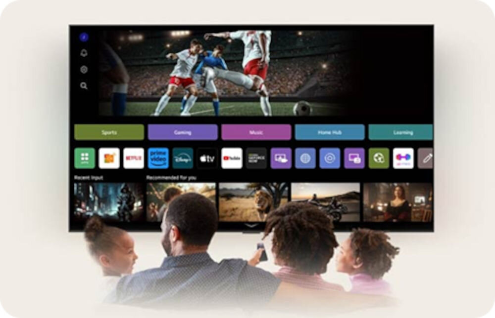 Na ekranie telewizora wyświetlany jest mecz piłki nożnej oraz interfejs z aplikacjami takimi jak Netflix, Prime Video, Disney+, YouTube. Przed telewizorem siedzi grupa osób oglądających program.