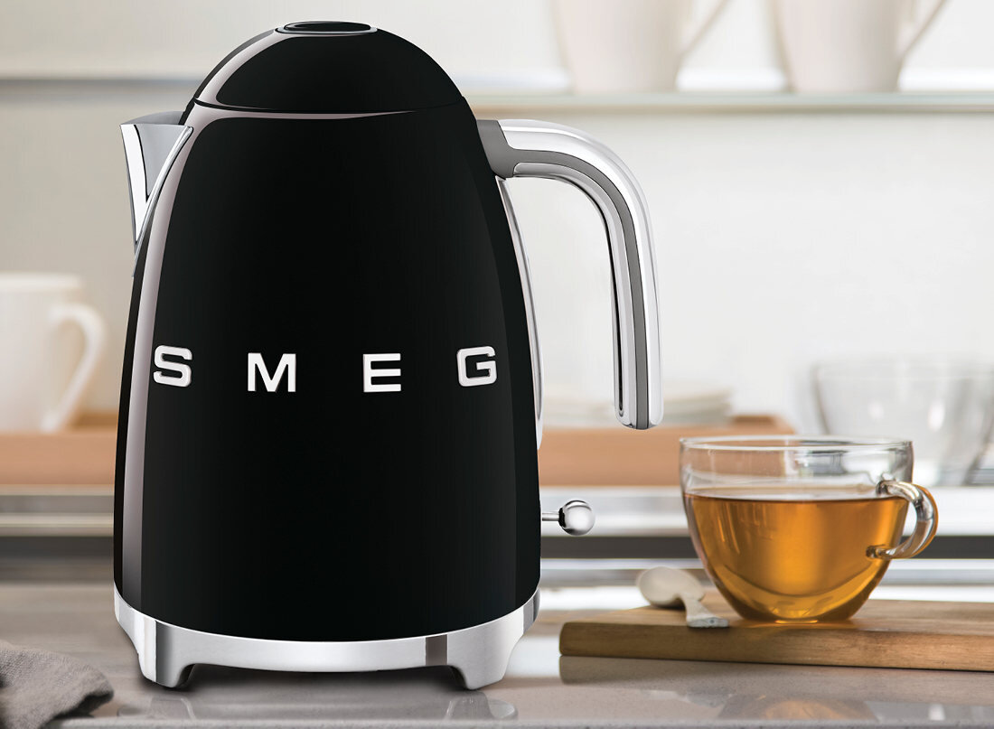 Czarny czajnik elektryczny z napisem \'SMEG\' na blacie kuchennym, obok szklanki z herbatą.