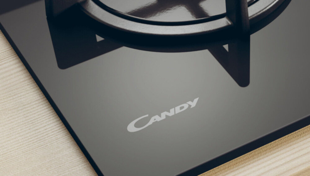 Czarna płyta gazowa z widocznym logo \'Candy\' na powierzchni. Na płycie znajduje się metalowy ruszt.