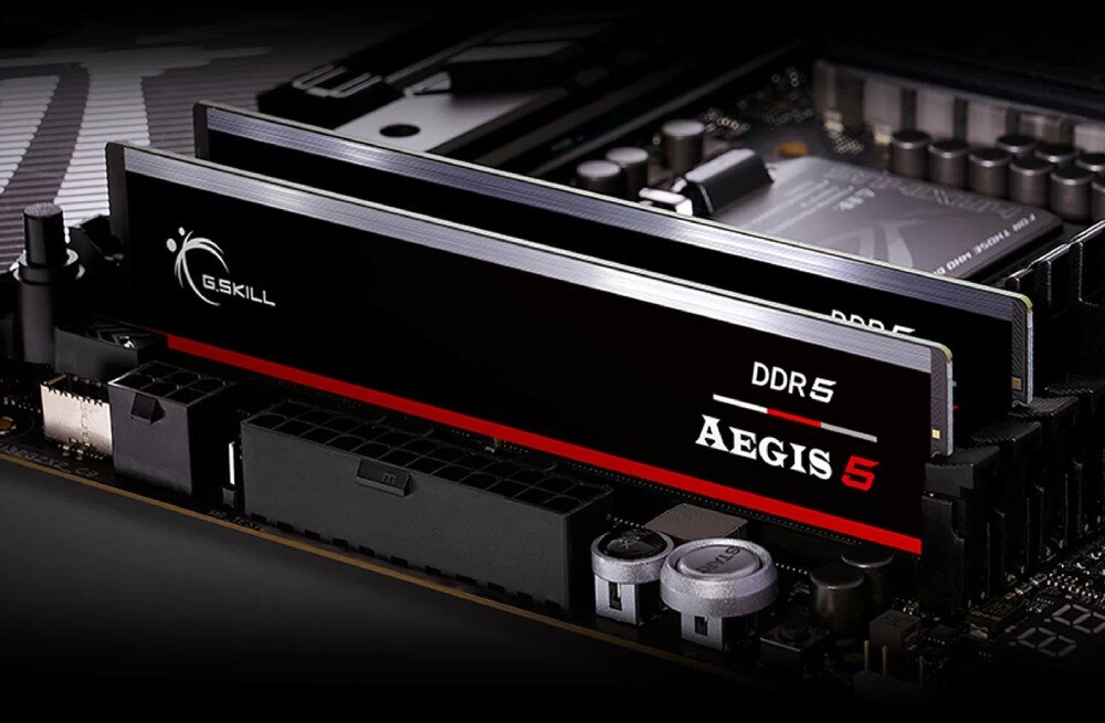 Na obrazie widoczne są dwa moduły pamięci RAM z oznaczeniami \'G.SKILL\' i \'DDR5 AEGIS 5\' zamontowane na płycie głównej.