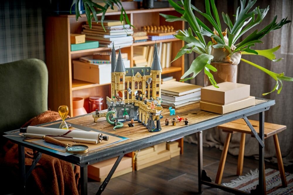 На столі стоїть модель замку LEGO, оточена книгами та рослиною в горщику. На задньому плані — книжкова полиця, заповнена книгами та коробками.