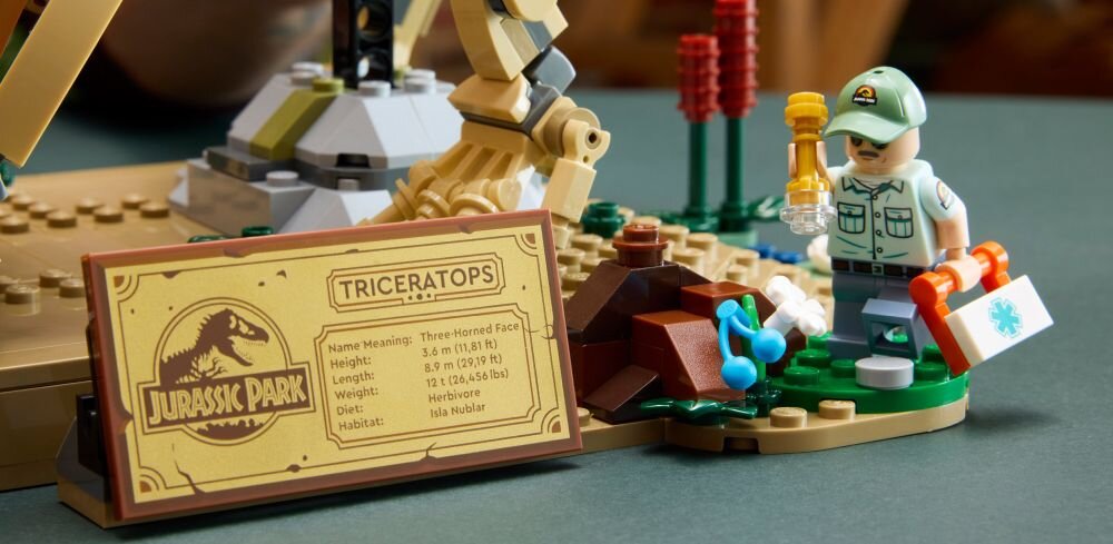 На зображенні фігурка LEGO у капелюсі з ліхтариком стоїть поруч із табличкою з написом «TRICERATOPS» та логотипом «PARK JURASSIC». Табличка містить інформацію про трицератопса, зокрема про його вагу, довжину, раціон та середовище проживання.