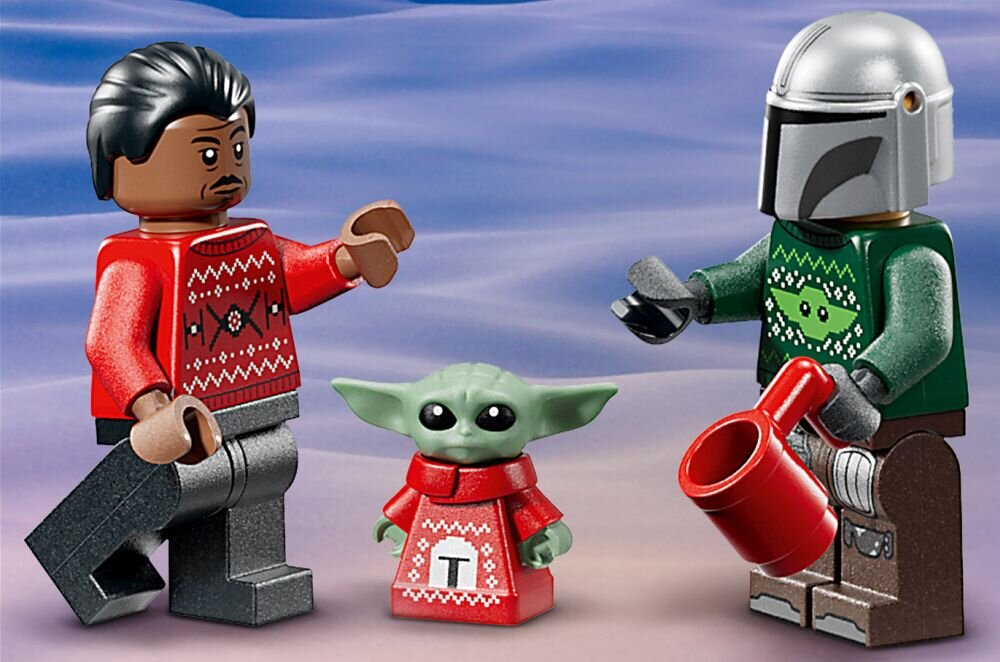 Na obrazie znajdują się trzy figurki LEGO w świątecznych swetrach, w tym jedna z zielonymi uszami i czerwoną koszulką z literą \'T\'. Jedna z figurek trzyma czerwony kubek.
