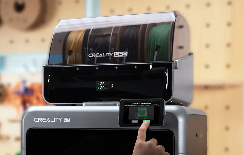 Na obrazie widoczna jest drukarka 3D z napisem \'CREALITY K2\' oraz pojemnik na filamenty z napisem \'CREALITY CFS\'. Na ekranie dotykowym wyświetlany jest tekst: \'Welcome to Creality 3D Printer\'.