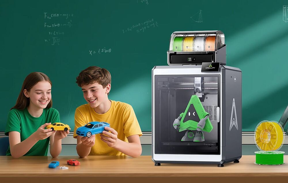 Na stole stoi drukarka 3D z przezroczystą obudową, w której widać zielony model robota. Obok siedzi dwoje dzieci trzymających kolorowe modele samochodów.
