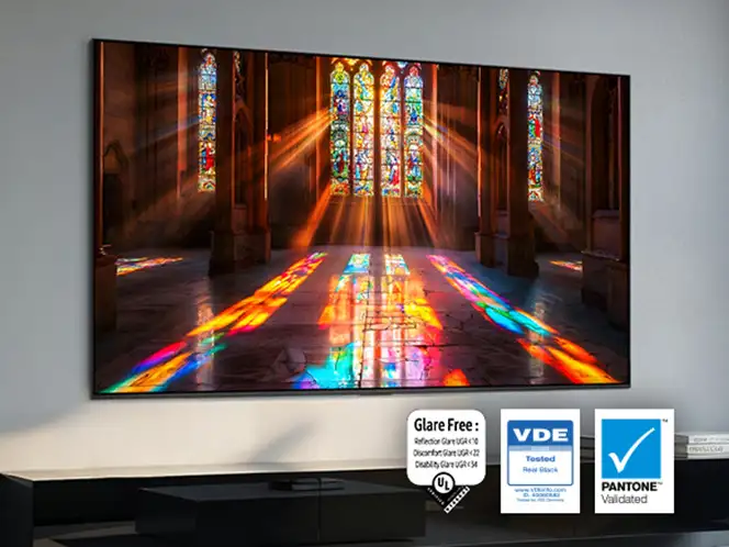 Telewizor wyświetla obraz wnętrza katedry z kolorowymi witrażami, przez które wpadają promienie światła. Na ekranie widoczne są trzy oznaczenia: \'Glare Free\', \'VDE Tested\' oraz \'PANTONE Validated\'.