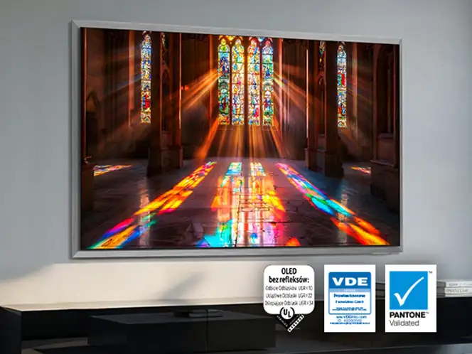 Telewizor wyświetla obraz wnętrza z kolorowymi witrażami, przez które wpadają promienie światła. Na dole ekranu widoczne są trzy oznaczenia: \'OLED bez refleksów\', \'VDE\', \'PANTONE Validated\'.
