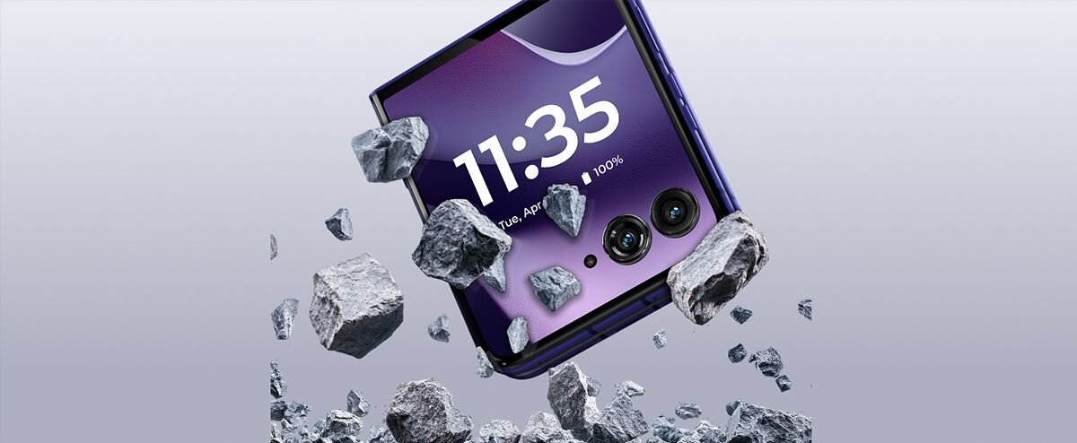 Smartfon z wyświetlaczem pokazującym godzinę 11:35, datę Tue, Apr 3 oraz poziom naładowania 100%, otoczony unoszącymi się kawałkami skał. Na obudowie widoczne są dwa obiektywy aparatu.
