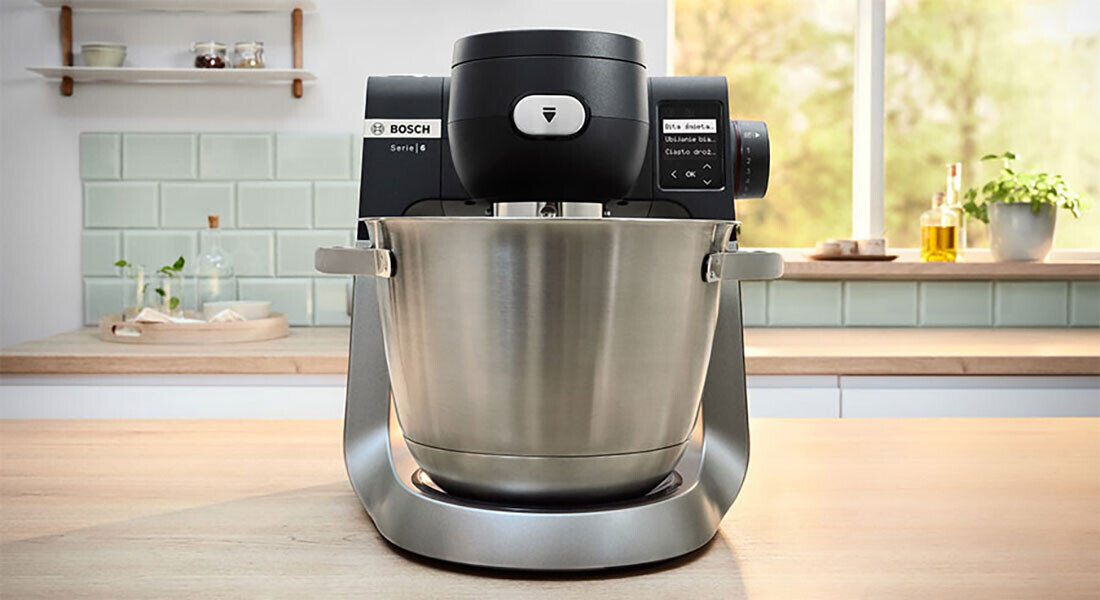 Na blacie kuchennym stoi robot kuchenny z dużą metalową misą. Na urządzeniu widoczne jest logo \'BOSCH\' oraz napis \'Series 6\'.