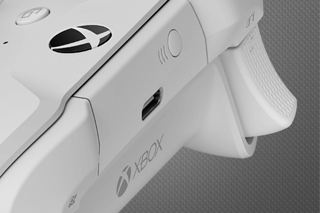 Zbliżenie na biały kontroler z widocznym logo Xbox oraz portem USB. Na powierzchni kontrolera znajdują się przyciski i tekstura uchwytu.