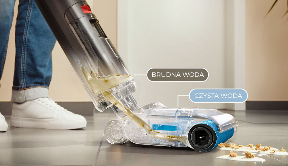 Odkurzacz mopujący z przezroczystym pojemnikiem na wodę, oznaczonym jako \'BRUDNA WODA\' i \'CZYSTA WODA\', zbiera rozlane płyny z podłogi. Obok urządzenia widoczne są białe buty osoby stojącej na podłodze.