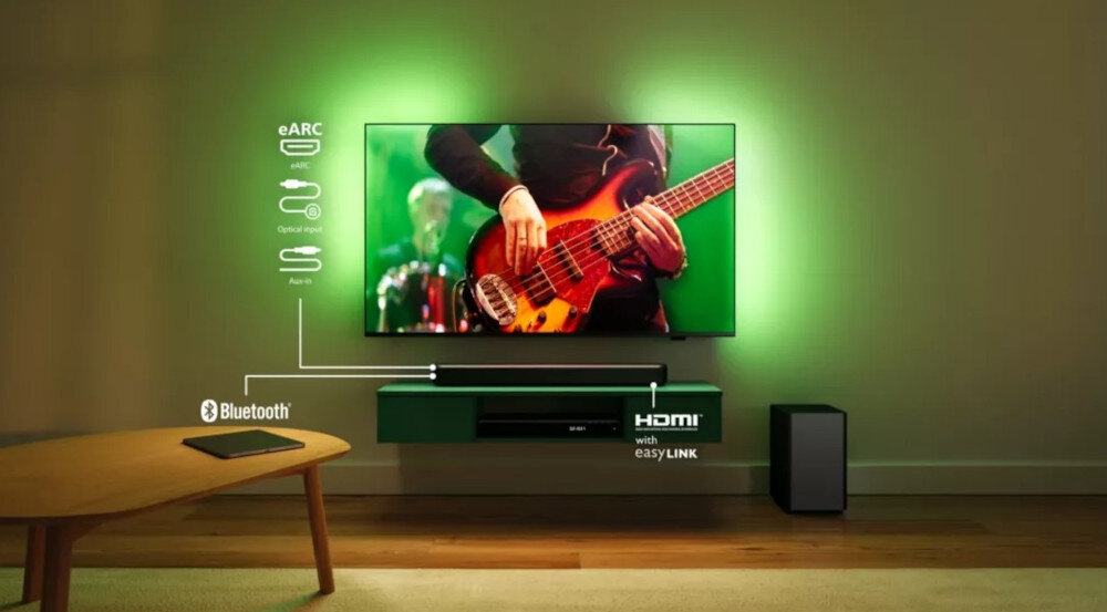 Na obrazie widać telewizor z zielonym podświetleniem, na którym wyświetlany jest muzyk grający na gitarze basowej. Pod telewizorem znajduje się soundbar, a obok niego bezprzewodowy subwoofer; widoczne są także ikony i napisy: eARC, Bluetooth, HDMI with easyLINK.