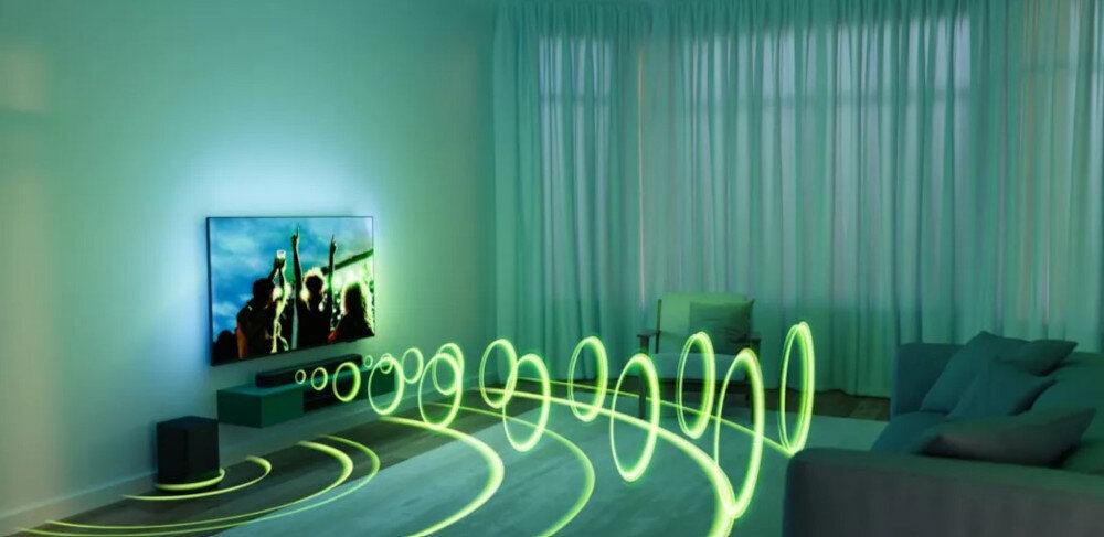 Pokój z telewizorem na ścianie, przed którym znajduje się soundbar i subwoofer. Zielone linie fal dźwiękowych wizualizują rozchodzenie się dźwięku w pomieszczeniu.