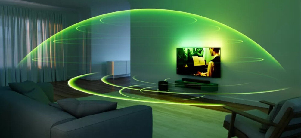 W salonie znajduje się telewizor z włączonym obrazem oraz soundbar umieszczony pod nim. Wokół telewizora i soundbara widoczne są zielone linie symbolizujące rozchodzący się dźwięk.
