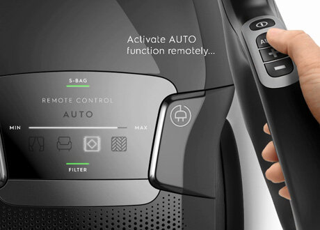 Zbliżenie na panel sterowania odkurzacza z napisem \'Activate AUTO function remotely...\'. Widoczne są przyciski i wskaźniki, w tym \'REMOTE CONTROL AUTO\', \'S-BAG\', \'FILTER\' oraz ikony trybów pracy.