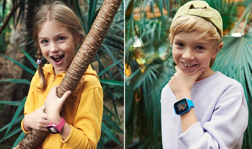 Dwoje dzieci pozuje w otoczeniu roślin, każde z nich nosi smartwatch na nadgarstku. Jedno dziecko ma różowy zegarek, a drugie niebieski.
