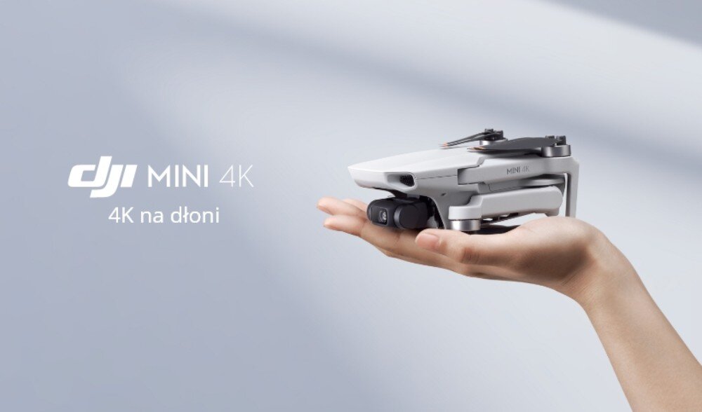 Osoba trzyma w dłoni małego drona w kolorze szarym. Obok widoczny jest tekst: \'DJI MINI 4K 4K na dłoni\'.