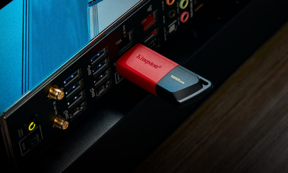 Czerwono-czarny pendrive z logo \'Kingston\' i oznaczeniem \'128GB\' jest podłączony do portu USB w komputerze. W tle widoczne są inne porty i złącza na obudowie komputera.