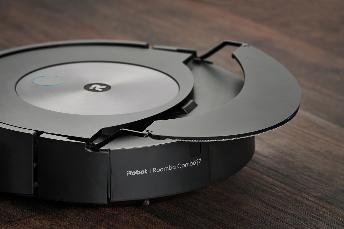 Na drewnianej powierzchni znajduje się robot sprzątający z otwartą pokrywą. Na obudowie widoczny jest napis \'iRobot Roomba Combo j7\'.