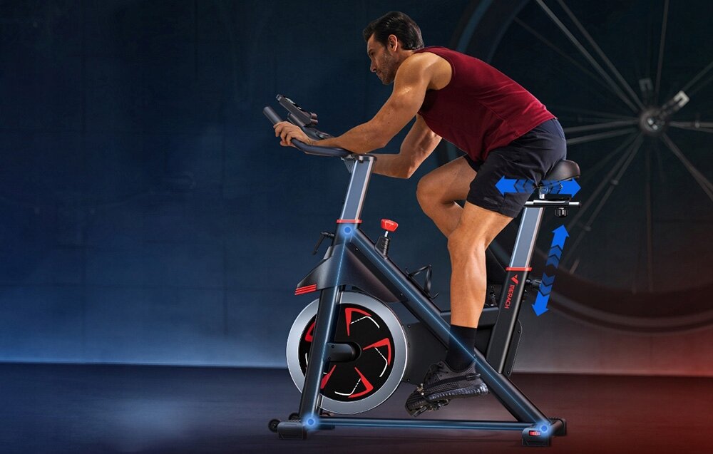 Osoba ćwiczy na rowerze treningowym w ciemnym pomieszczeniu. Rower ma nowoczesny design z czerwonymi i czarnymi elementami.
