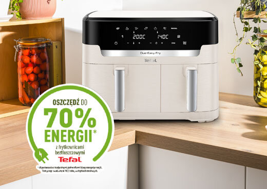 Na blacie kuchennym stoi frytkownica beztłuszczowa z panelem dotykowym i dwoma uchwytami. Obok znajduje się zielony znak z napisem \'OSZCZĘDŹ DO 70% ENERGII z frytkownicami beztłuszczowymi Tefal\'.