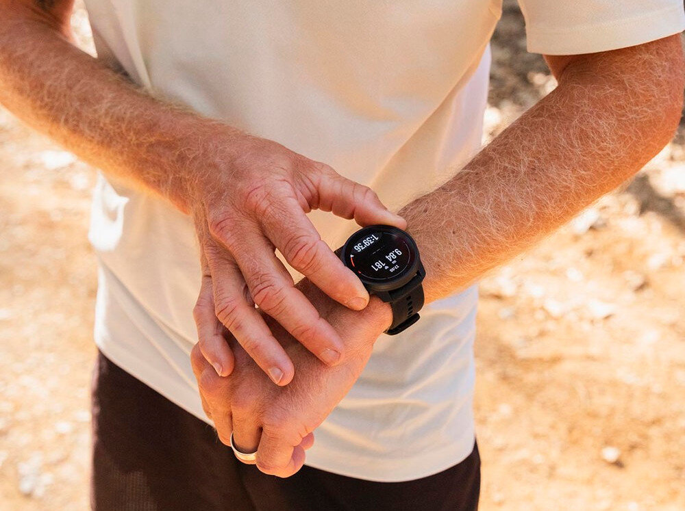 Osoba nosi czarny smartwatch na nadgarstku, na ekranie widoczny jest tekst: \'85 BEATS\'.