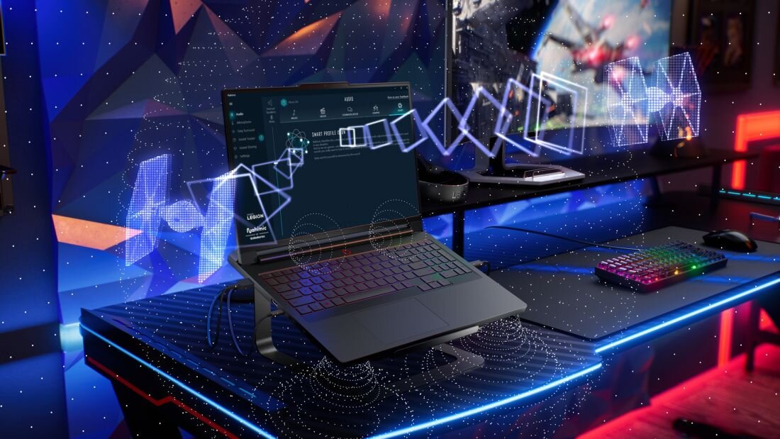 Na biurku znajduje się laptop z podświetlaną klawiaturą, a na ekranie widoczny jest interfejs oprogramowania. W tle widać monitor z dynamiczną grafiką oraz klawiaturę z kolorowym podświetleniem.