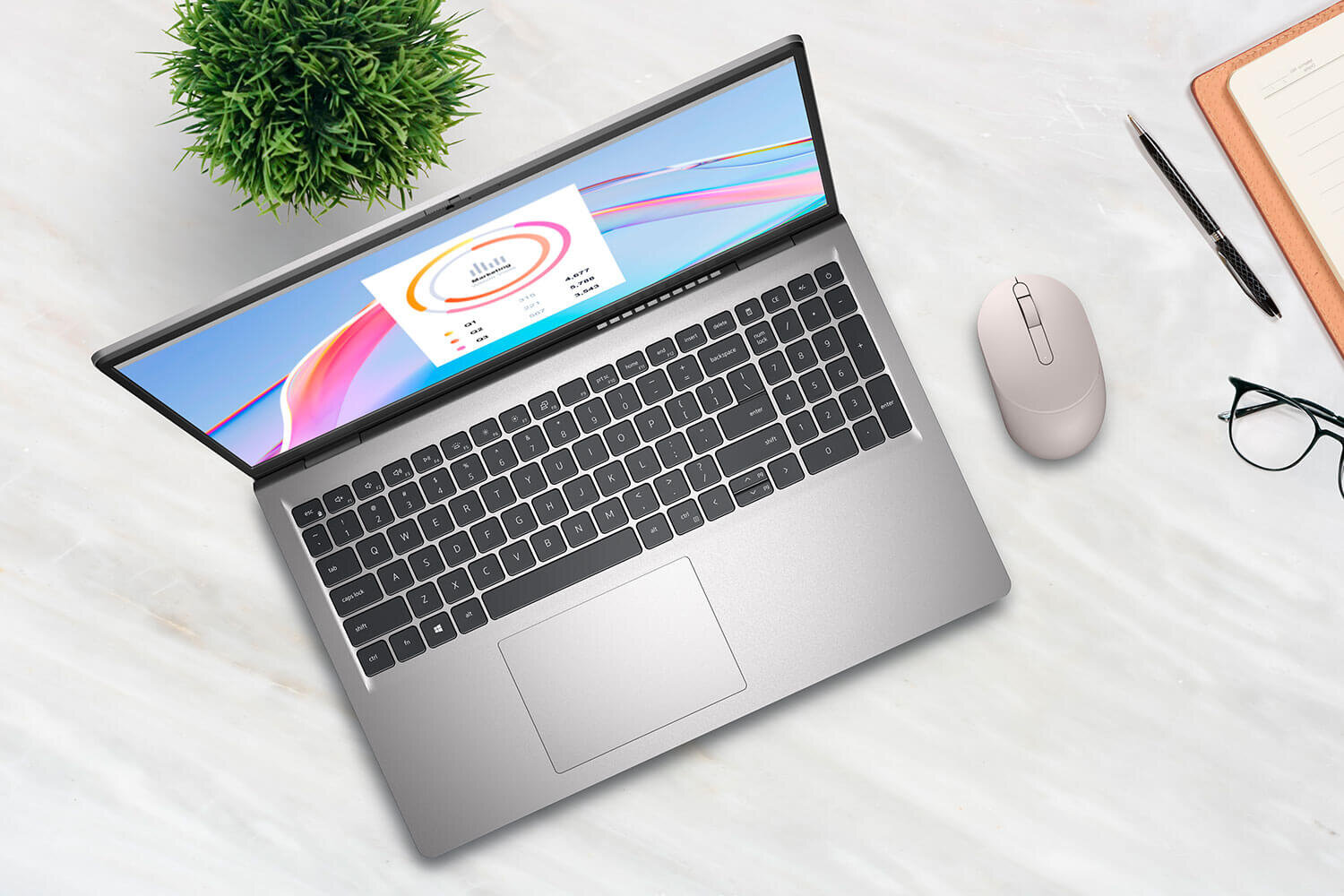 Na obrazie znajduje się otwarty laptop z widocznym ekranem, na którym wyświetlany jest kolorowy wykres. Obok laptopa leży myszka, okulary, długopis i notes, a w tle widoczna jest zielona roślina.