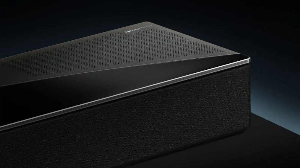 Czarny soundbar z perforowaną górną powierzchnią i logo producenta. Urządzenie ma nowoczesny design z metalicznymi akcentami.