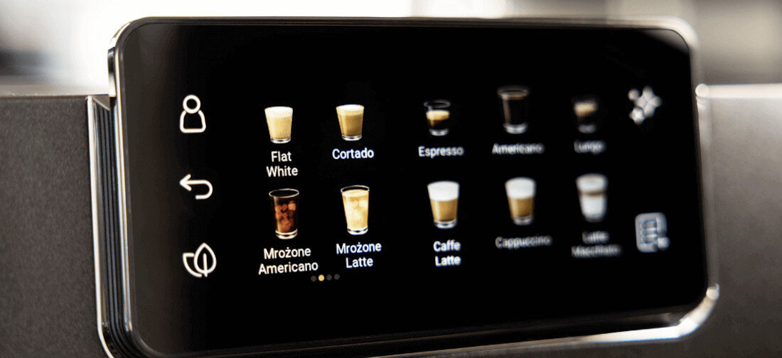 Panel dotykowy ekspresu do kawy z ikonami różnych napojów, takich jak Flat White, Cortado, Espresso, Americano, Lungo, Mrożone Americano, Mrożone Latte, Caffe Latte, Cappuccino i Latte Macchiato. Obok ikon znajdują się symbole użytkownika i strzałki.