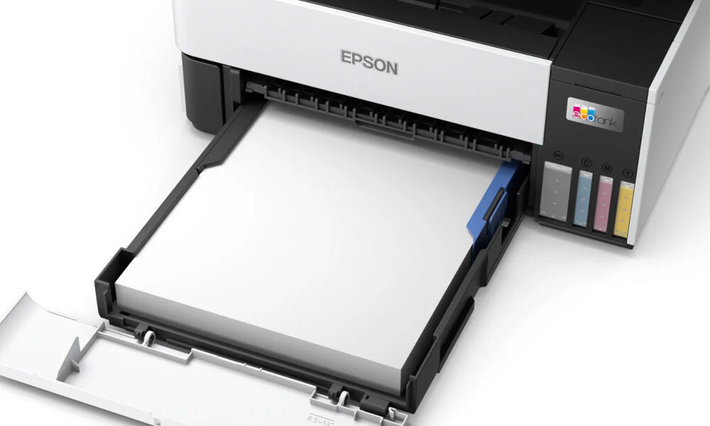 Na obrazie widoczne jest urządzenie wielofunkcyjne z logo \'EPSON\' na górze oraz kolorowymi wskaźnikami poziomu tuszu z boku. Tacka na papier jest wysunięta, a na niej znajduje się stos białych arkuszy papieru.
