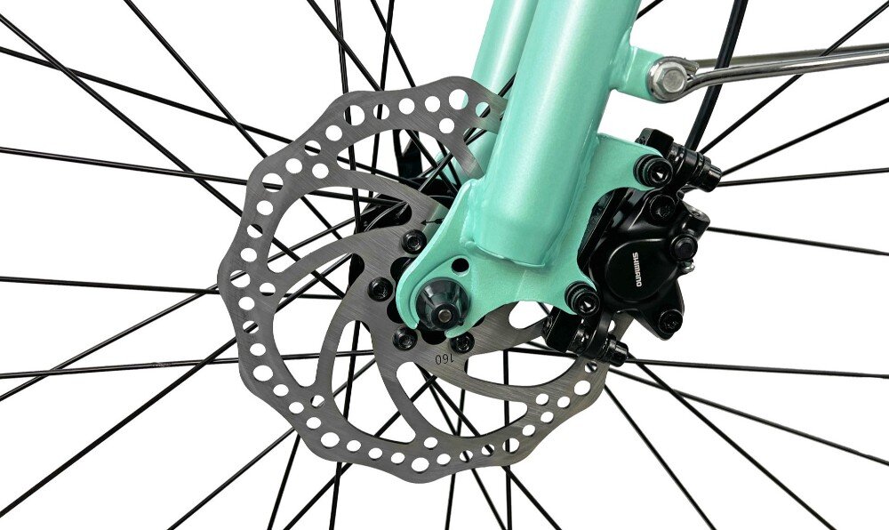 Zbliżenie na tarczę hamulcową roweru w kolorze akwamaryny z widocznym mechanizmem hamulcowym. Tarcza ma liczne otwory i jest przymocowana do widelca roweru.