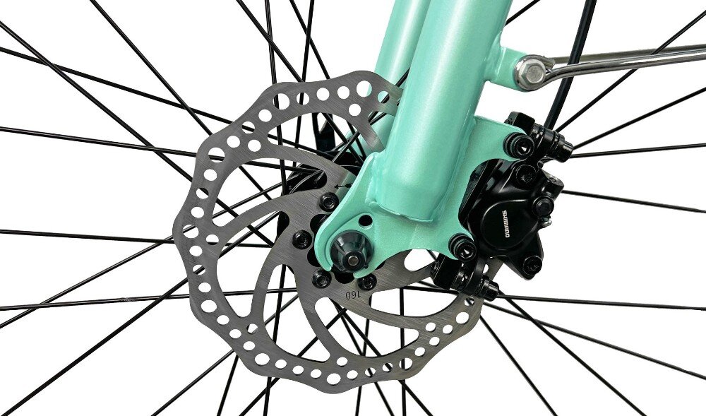 Zbliżenie na tarczę hamulcową roweru w kolorze akwamaryny z widocznym zaciskiem hamulcowym z napisem \'SHIMANO\'.
