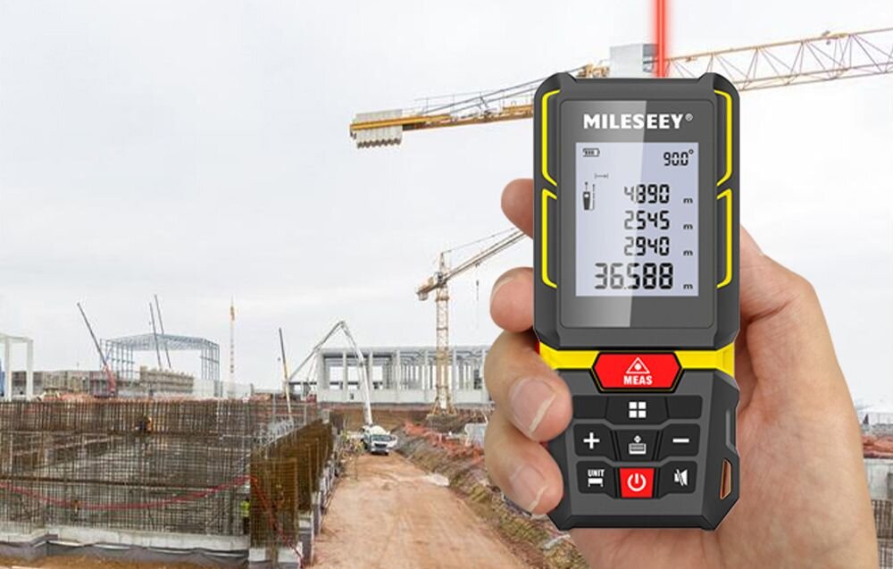 Dalmierz laserowy MILESEEY G7 100m, Mileseey, dłoń, budowa, żurawie, Urządzenie Mileseey trzymane w ręku na tle placu budowy z żurawiami wieżowymi i betonowymi konstrukcjami.