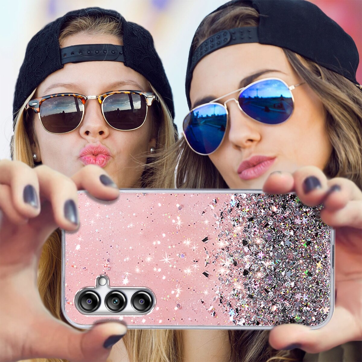 Dwie osoby w okularach przeciwsłonecznych trzymają telefon z różowym, brokatowym etui. Etui ma trzy otwory na aparaty fotograficzne.