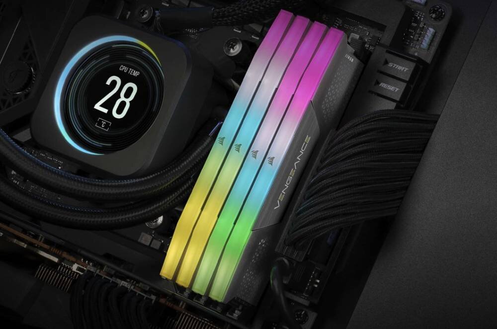 Obraz przedstawia wnętrze komputera z zainstalowanymi modułami pamięci RAM z podświetleniem RGB w kolorach tęczy. Na wyświetlaczu widoczna jest temperatura procesora: \'CPU TEMP 28\'.