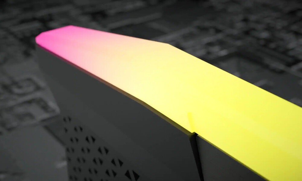 Obraz przedstawia fragment urządzenia z podświetleniem RGB, które przechodzi z różowego w żółty kolor. Tło jest rozmyte i szare, co podkreśla kolorowe podświetlenie.
