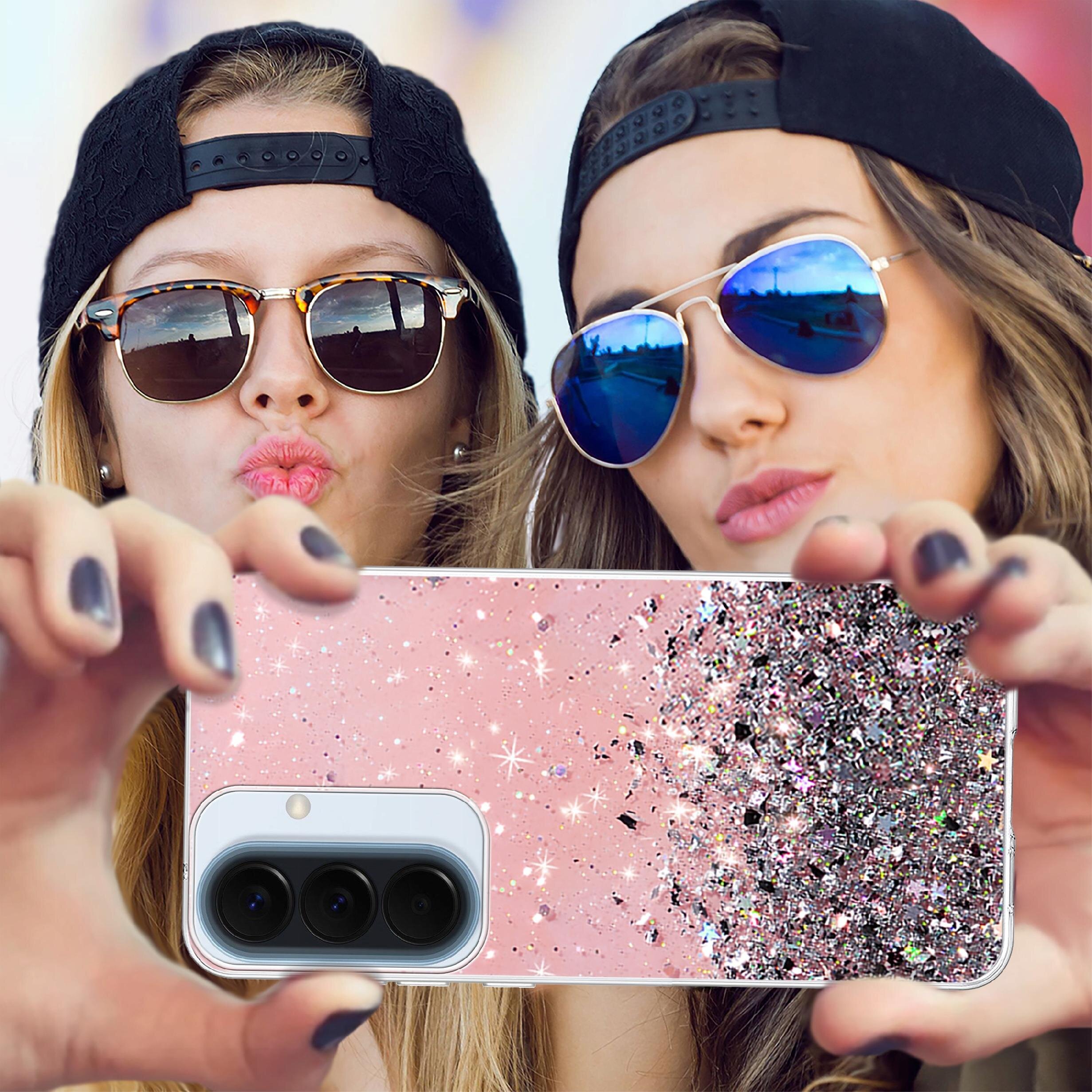 Dwie osoby w okularach przeciwsłonecznych trzymają telefon z różowym etui ozdobionym brokatem i błyszczącymi elementami. Etui posiada wycięcie na aparat z trzema obiektywami.