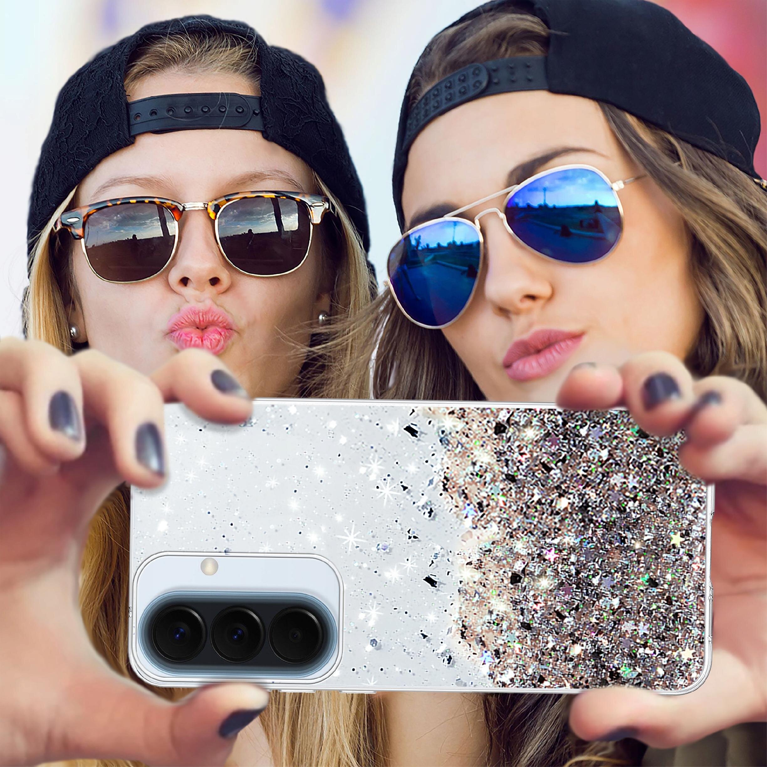 Dwie osoby w okularach przeciwsłonecznych trzymają telefon z etui pokrytym brokatem. Etui ma wycięcie na aparat z trzema obiektywami.