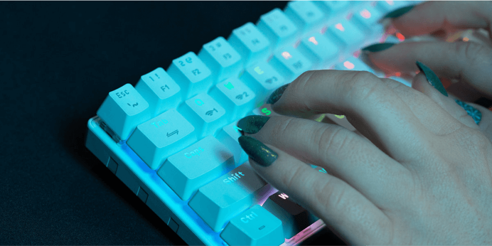 Osoba pisze na białej klawiaturze z podświetleniem RGB. Widoczne są klawisze z oznaczeniami takimi jak \'Shift\' i \'Ctrl\'.